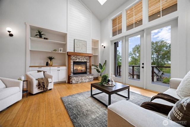 living room with a fireplace, light wood finished floors, high vaulted ceiling, and built in shelves