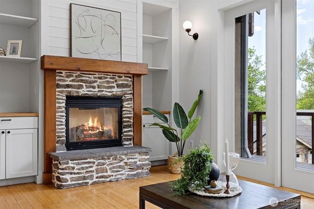 living room with built in features, wood finished floors, and a stone fireplace