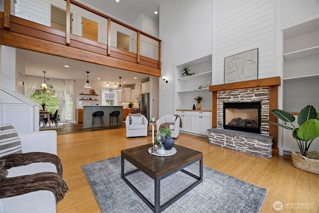 living room with a fireplace, light wood finished floors, a towering ceiling, and built in features