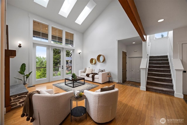 living area featuring stairway, a skylight, high vaulted ceiling, and light wood-style flooring