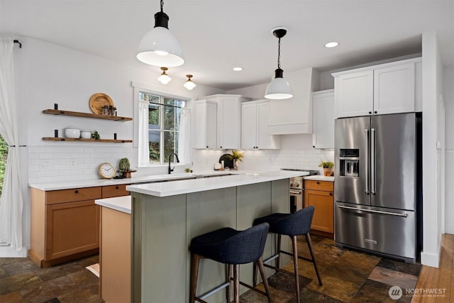 kitchen with high end fridge, a sink, a kitchen breakfast bar, backsplash, and light countertops