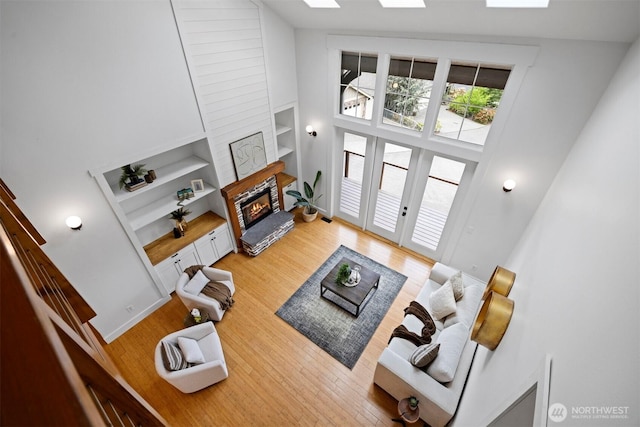 living room featuring light wood finished floors, french doors, high vaulted ceiling, a glass covered fireplace, and built in shelves