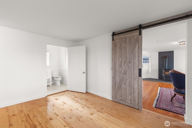 275 State Route 409, Cathlamet, WA 98612 - bedroom featuring a barn door, a wood stove, wood-type flooring, ensuite bath, and baseboards