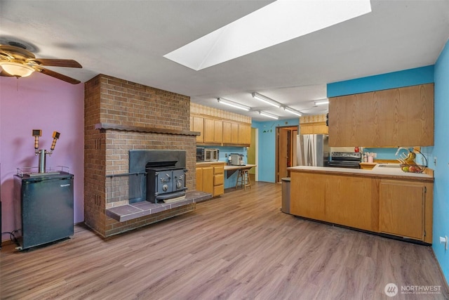 4901 Delta Ln SE, Tumwater, WA 98501 - kitchen with appliances with stainless steel finishes, a wood stove, light wood-type flooring, a skylight, and a peninsula