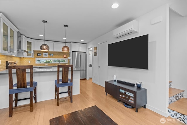 kitchen featuring freestanding refrigerator, light wood-style floors, a kitchen breakfast bar, wall chimney exhaust hood, and a wall unit AC
