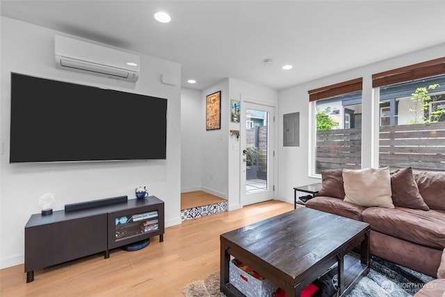 living room with a wall unit AC, electric panel, baseboards, recessed lighting, and light wood-style flooring