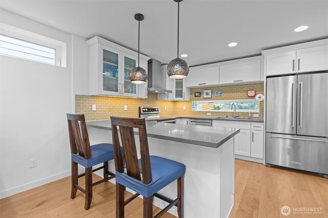 kitchen with a breakfast bar area, wall chimney range hood, white cabinets, a sink, and stainless steel appliances