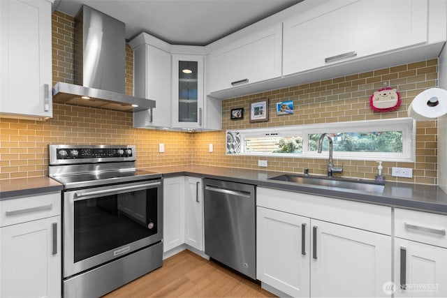 kitchen with wall chimney range hood, appliances with stainless steel finishes, dark countertops, and a sink