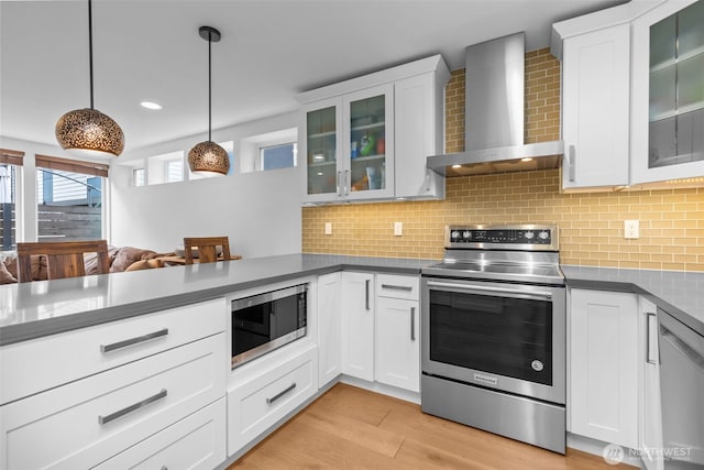 kitchen with backsplash, dark countertops, appliances with stainless steel finishes, white cabinetry, and wall chimney exhaust hood