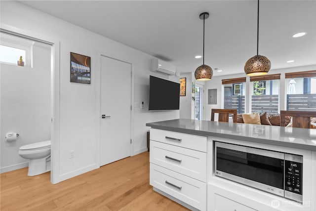 kitchen featuring a wall mounted air conditioner, recessed lighting, white cabinetry, stainless steel microwave, and light wood-style flooring