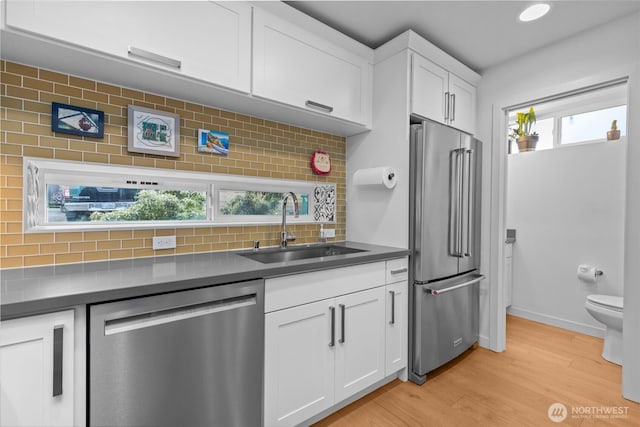 kitchen featuring white cabinetry, a sink, light wood finished floors, backsplash, and stainless steel appliances