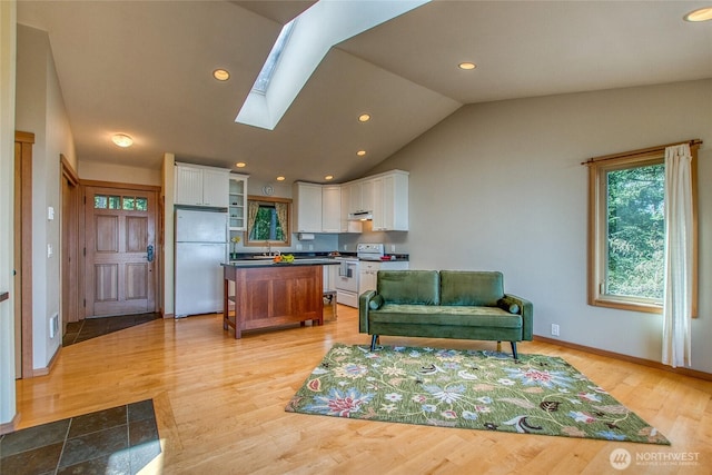kitchen with dark countertops, white cabinets, under cabinet range hood, white electric stove, and freestanding refrigerator