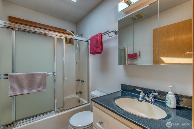 bathroom featuring vanity, toilet, bath / shower combo with glass door, and visible vents