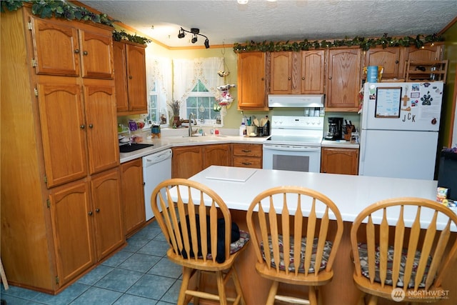 kitchen featuring a textured ceiling, light countertops, white appliances, tile patterned floors, and under cabinet range hood