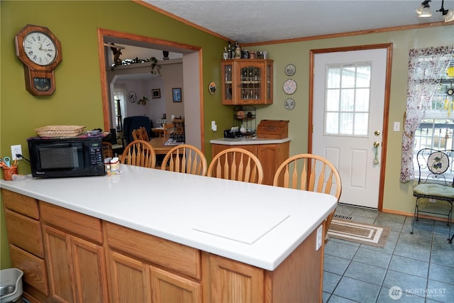kitchen with light countertops, vaulted ceiling, light tile patterned flooring, a peninsula, and black microwave