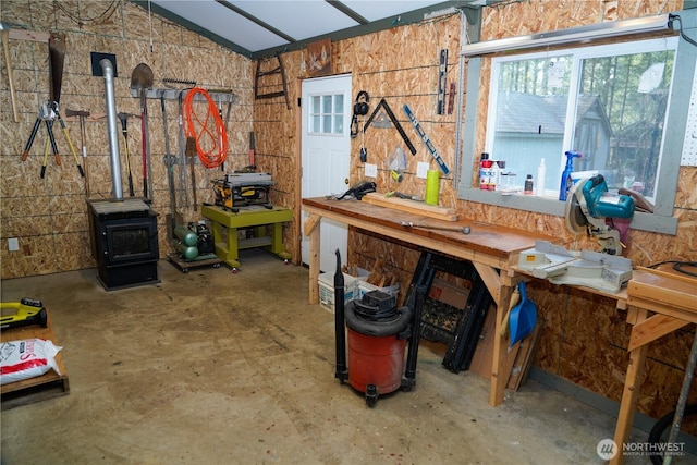 miscellaneous room with a wood stove, concrete floors, vaulted ceiling, and a workshop area