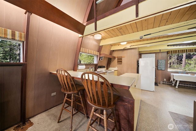dining space featuring beamed ceiling, baseboard heating, and wood walls