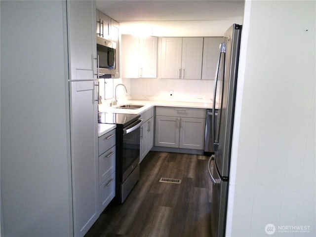 kitchen featuring light countertops, stainless steel appliances, dark wood-type flooring, a sink, and gray cabinetry