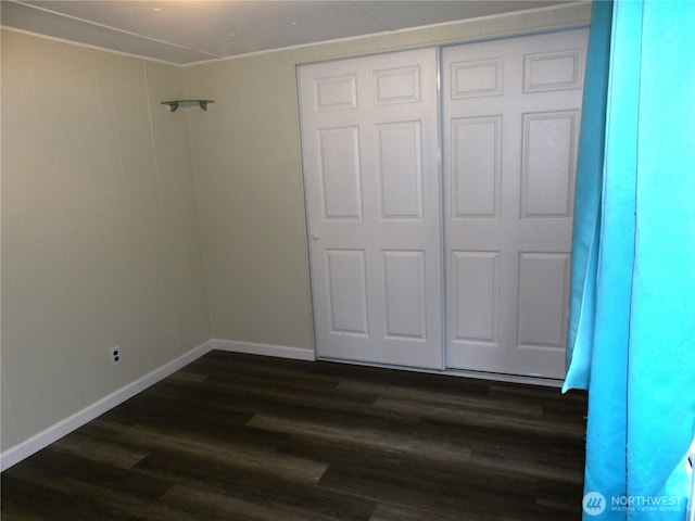 unfurnished bedroom featuring dark wood-type flooring, a closet, and baseboards