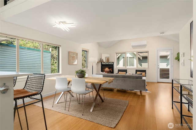 3924 S Brandon St Unit A, Seattle, WA 98118 - dining area with light wood-style flooring, a wall unit AC, baseboards, lofted ceiling, and a warm lit fireplace
