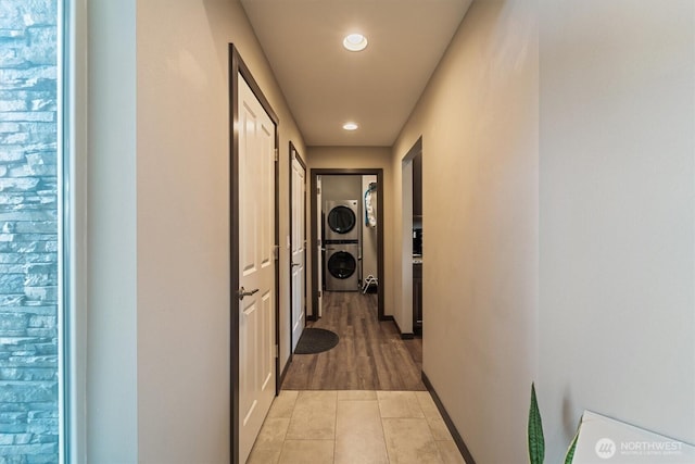 corridor featuring baseboards, recessed lighting, stacked washing maching and dryer, and light tile patterned flooring