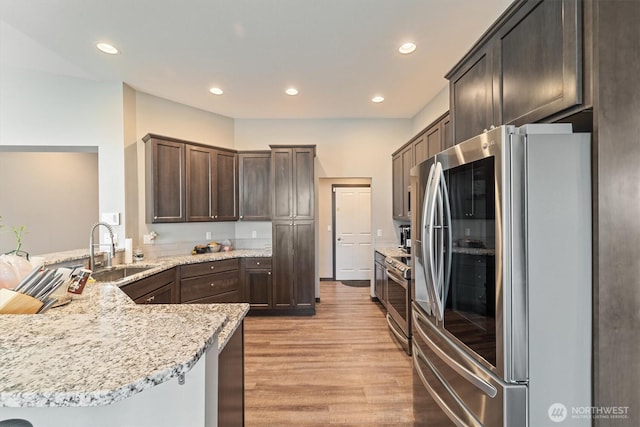 kitchen with a peninsula, light wood-style flooring, dark brown cabinets, stainless steel appliances, and a sink
