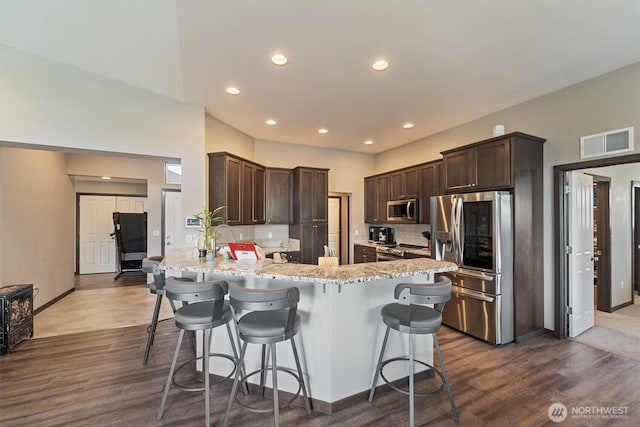 kitchen with a peninsula, appliances with stainless steel finishes, visible vents, and dark brown cabinetry