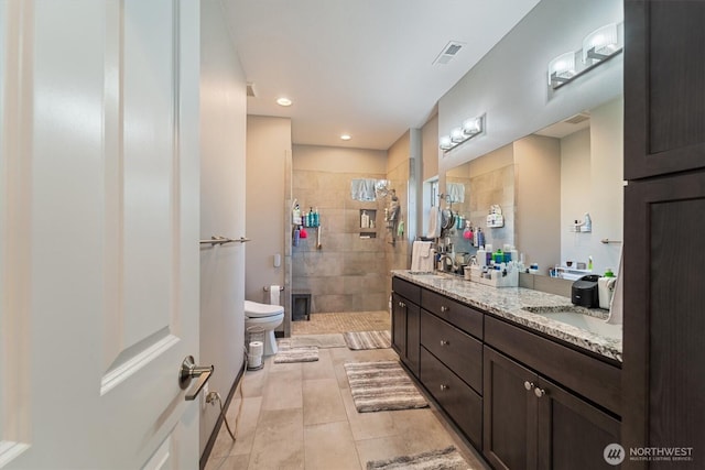 bathroom featuring visible vents, toilet, a sink, a stall shower, and double vanity