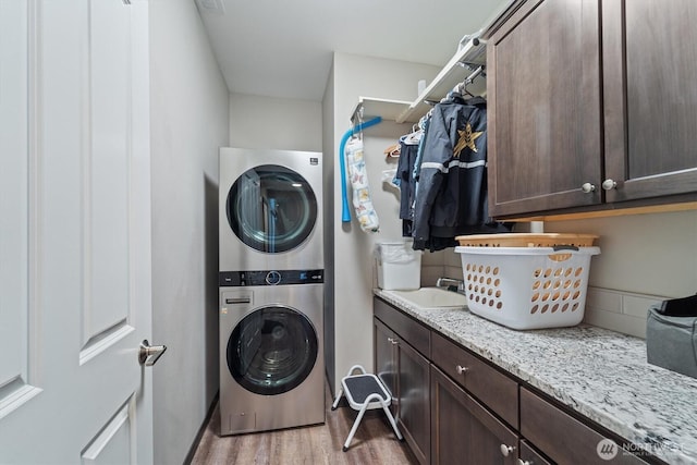 clothes washing area featuring stacked washer and dryer, a sink, cabinet space, and wood finished floors