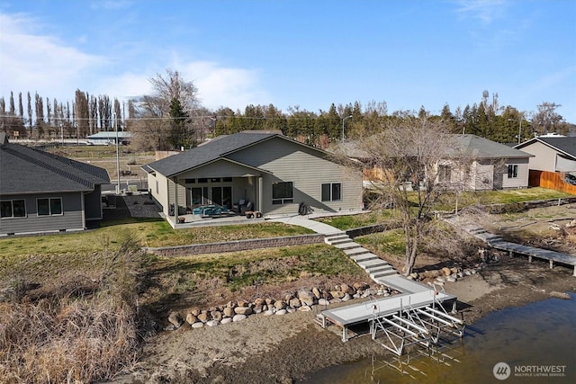 rear view of property with a patio, boat lift, a water view, and a yard