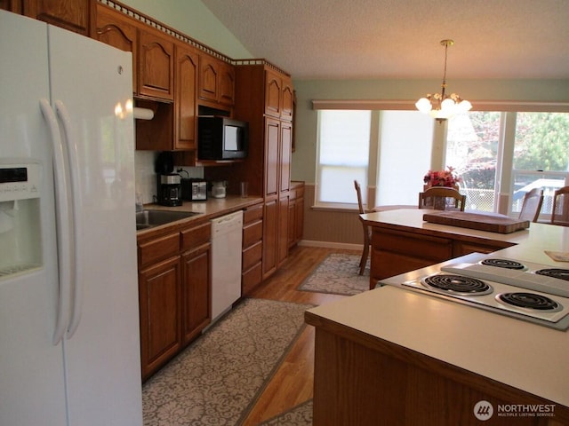 kitchen with brown cabinets, a sink, light wood finished floors, white appliances, and a chandelier
