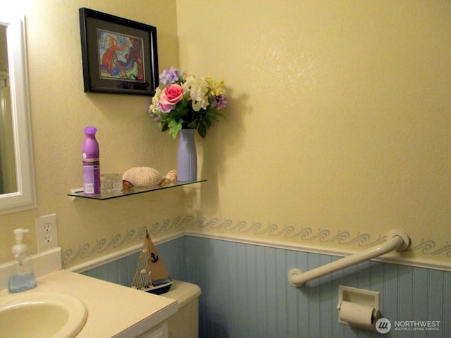 half bath with a wainscoted wall, vanity, and toilet