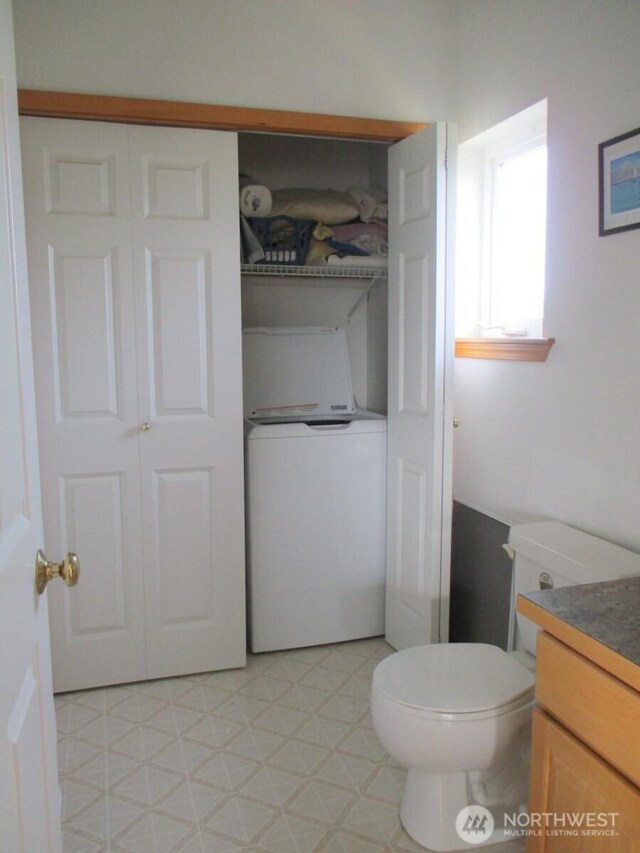 half bath featuring tile patterned floors, washer / dryer, toilet, and vanity