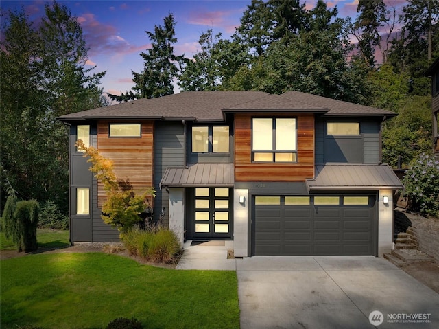 view of front of home featuring a garage, a front yard, concrete driveway, a standing seam roof, and metal roof