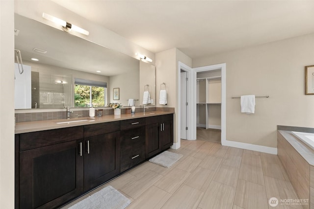 bathroom featuring double vanity, tiled tub, a spacious closet, a sink, and a tile shower