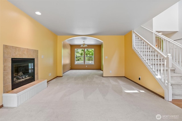 unfurnished living room featuring carpet floors, a fireplace, baseboards, stairway, and arched walkways