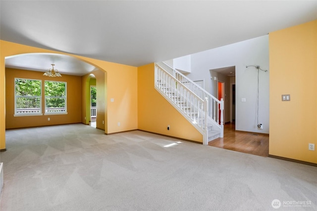unfurnished living room with carpet floors, arched walkways, baseboards, and stairway