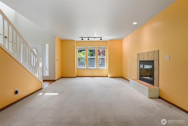 unfurnished living room with carpet floors, stairs, baseboards, and a tiled fireplace