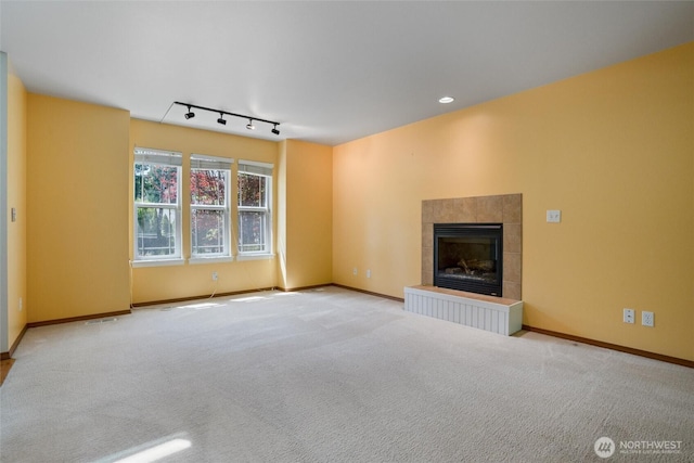 unfurnished living room featuring a tiled fireplace, carpet, baseboards, and rail lighting