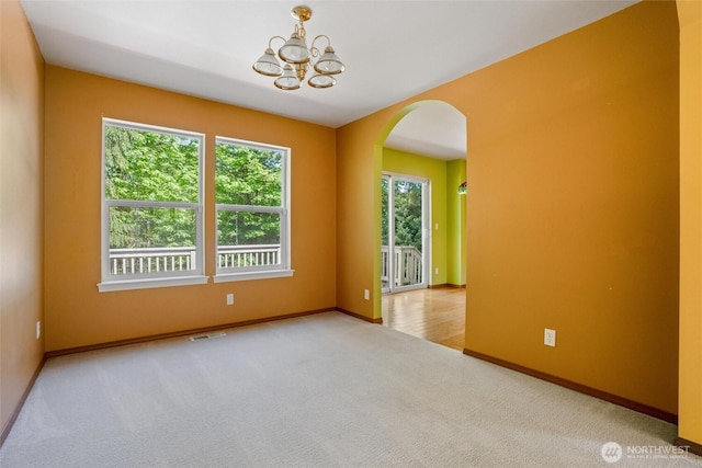 carpeted spare room featuring plenty of natural light, arched walkways, a chandelier, and visible vents