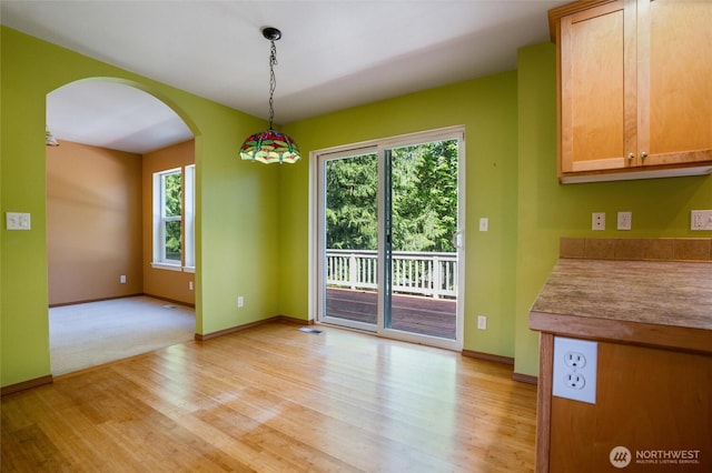 unfurnished dining area featuring a healthy amount of sunlight, arched walkways, baseboards, and light wood-style floors