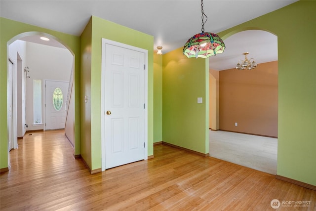 unfurnished room with arched walkways, baseboards, an inviting chandelier, and light wood-style flooring
