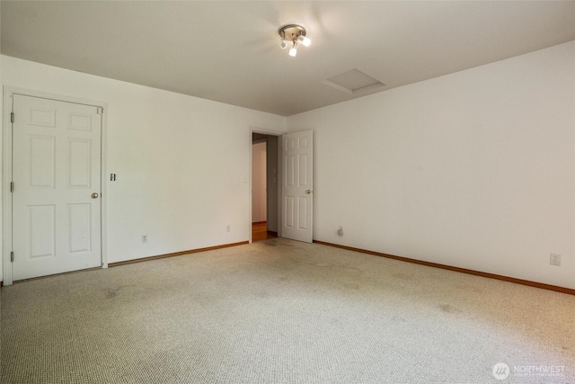 empty room with baseboards, attic access, and light carpet