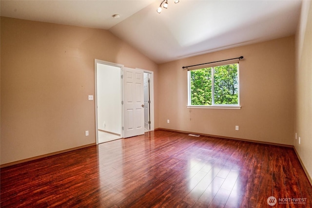 unfurnished room featuring baseboards, vaulted ceiling, wood finished floors, and visible vents