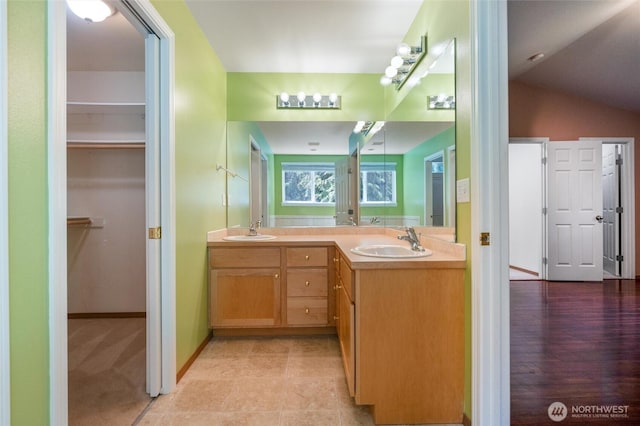 full bath featuring double vanity, a sink, a walk in closet, and lofted ceiling