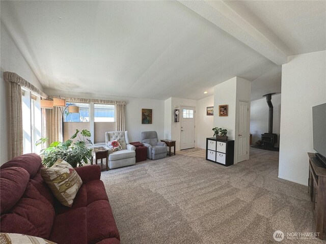 carpeted living area featuring vaulted ceiling with beams and a wood stove
