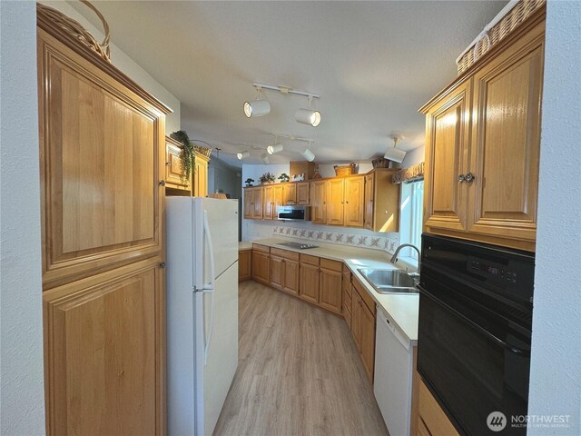 kitchen with light countertops, a sink, black appliances, and light wood finished floors