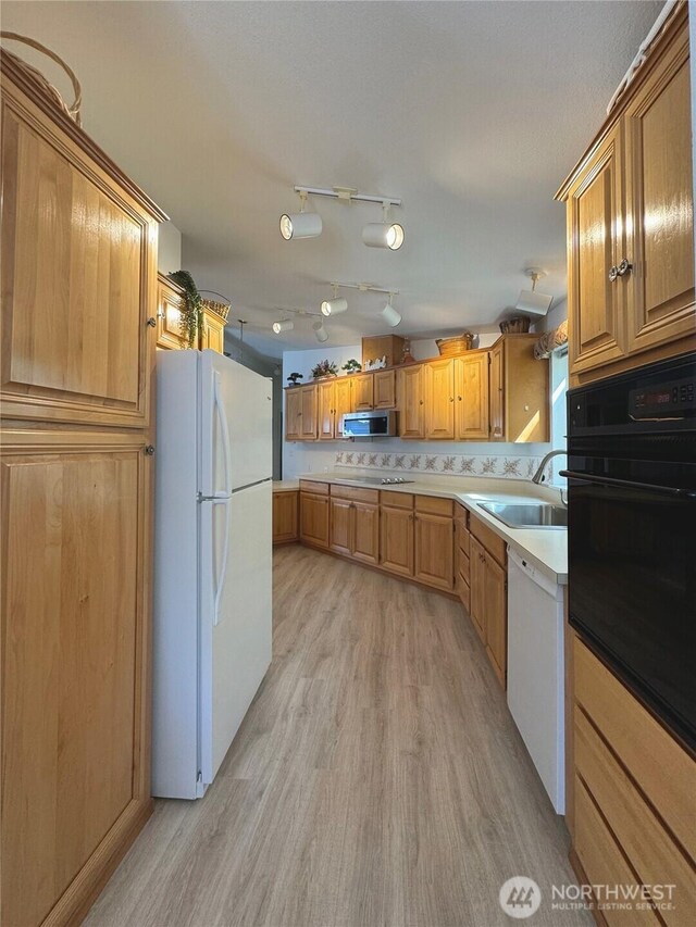 kitchen featuring light countertops, a sink, brown cabinetry, black appliances, and light wood-style floors