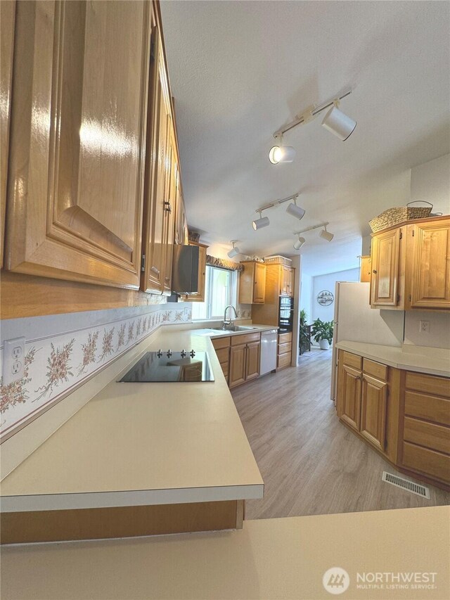 kitchen with light countertops, dishwashing machine, black electric cooktop, brown cabinetry, and visible vents