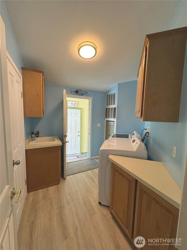 laundry room with a textured ceiling, light wood-style flooring, a sink, washer and dryer, and cabinet space